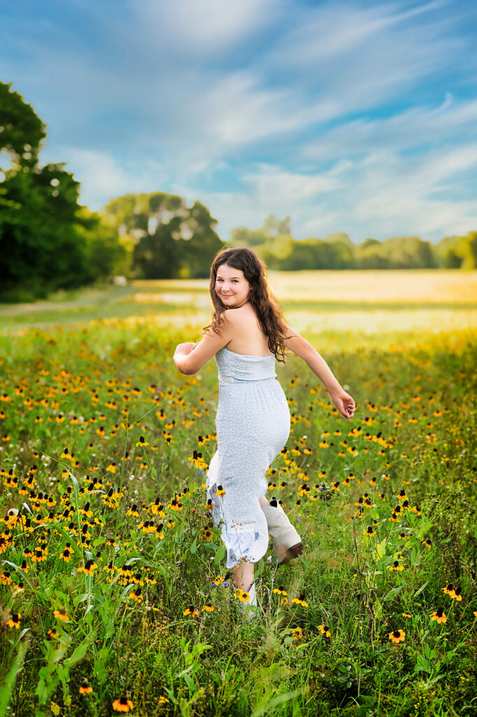 young girl in a light blue dress walking through a wildflower field during her Fort Worth senior portrait session
