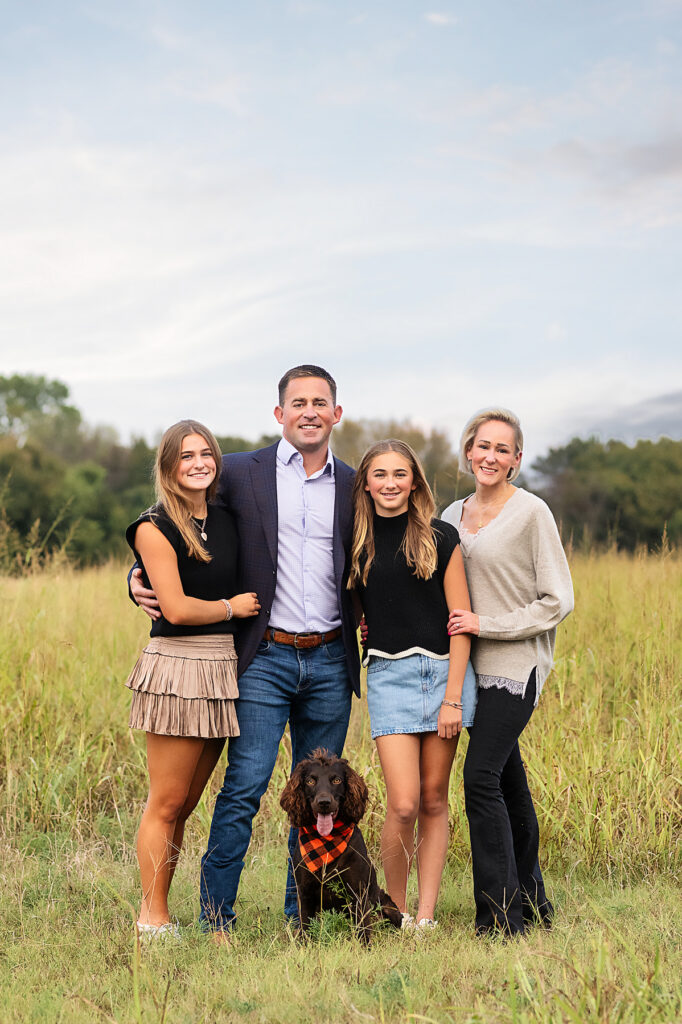 Family of four smiling together in a grassy field during a Fort Worth family portrait session