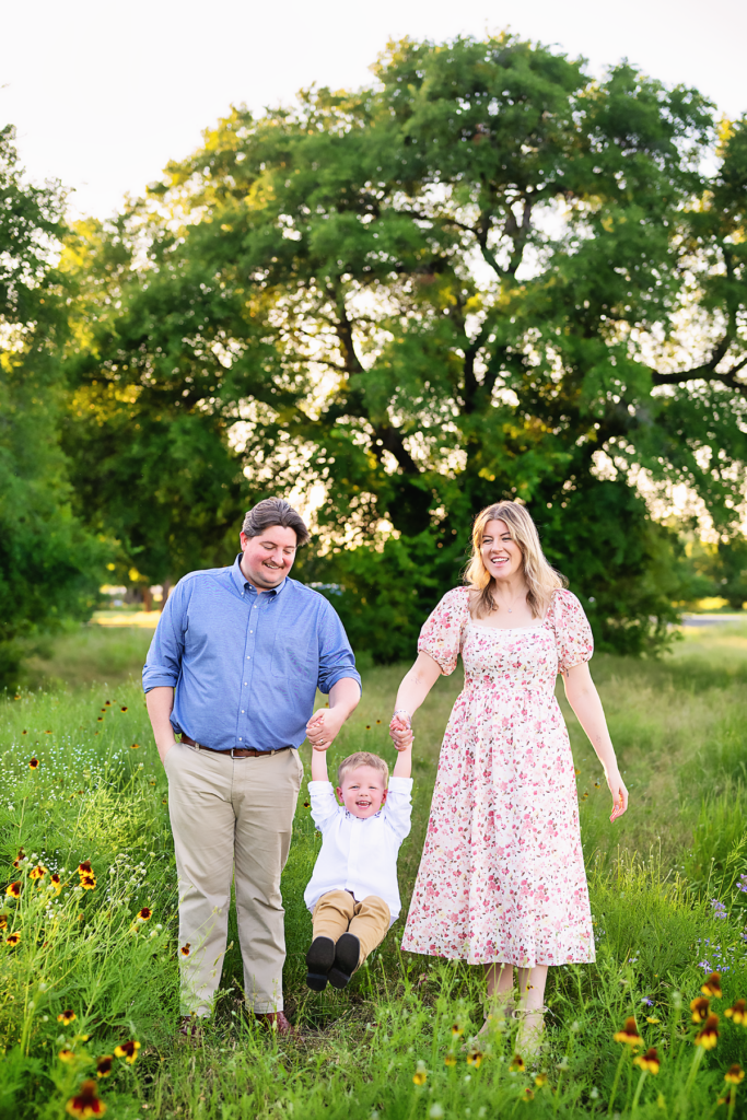 Parents walking through a green field with their young child during a Fort Worth family photography session