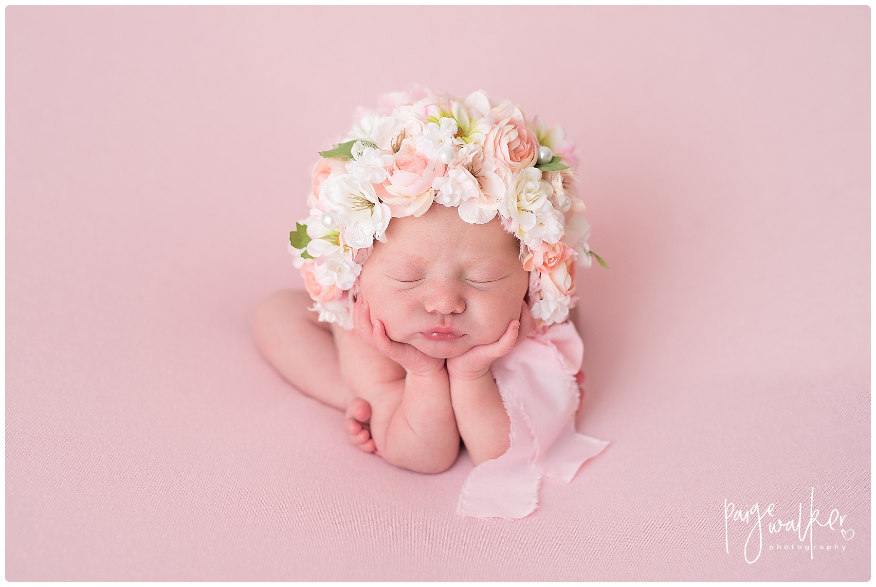 newborn girl in the froggy pose with a flower bonnet on